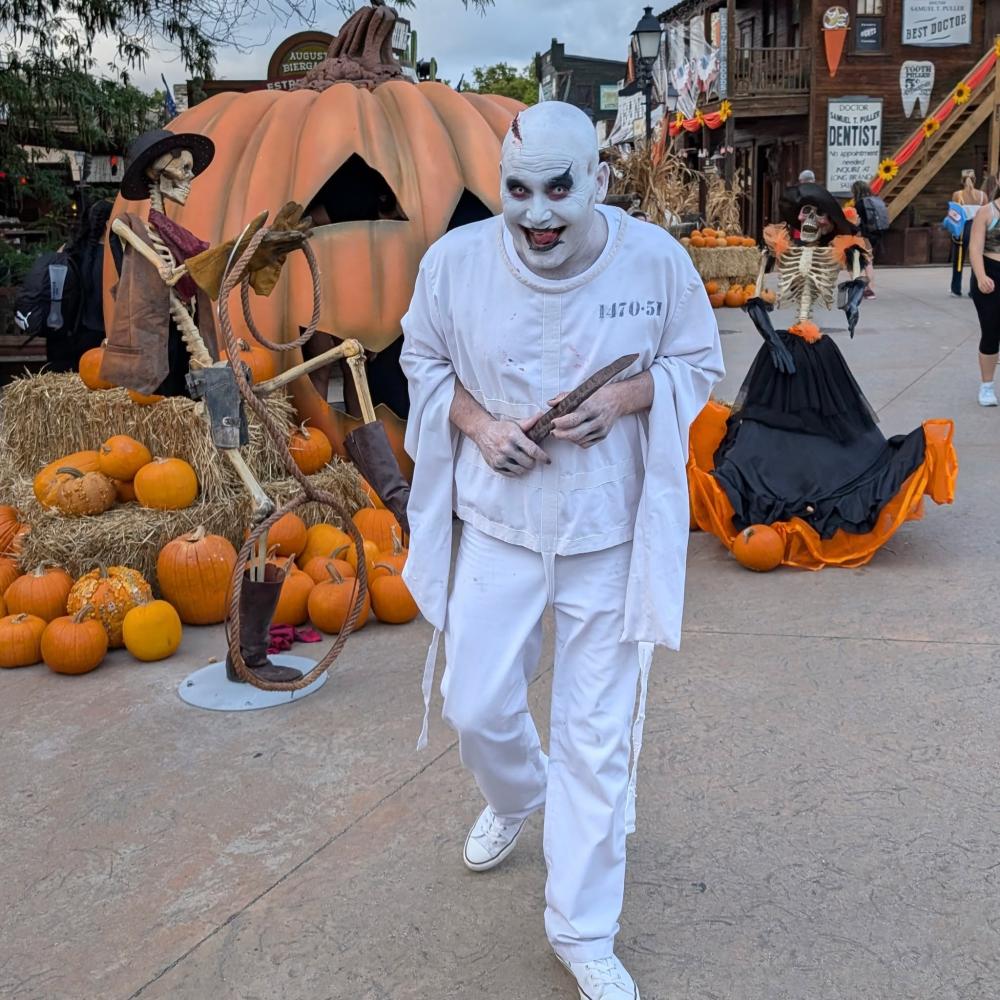 Actor caracterizado de Halloween junto a calabazas y esqueletos decorativos en el parque